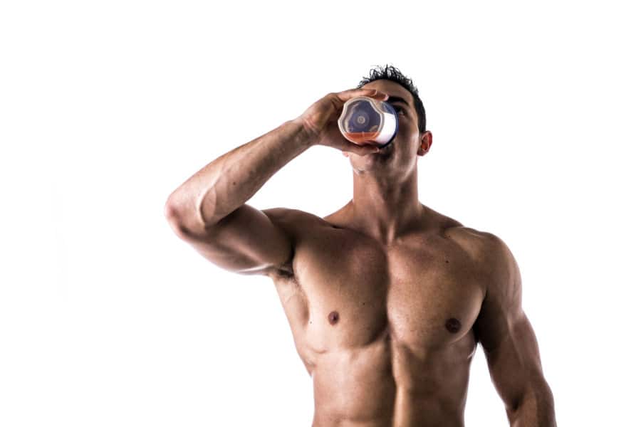 Muscular shirtless male bodybuilder drinking protein shake from blender